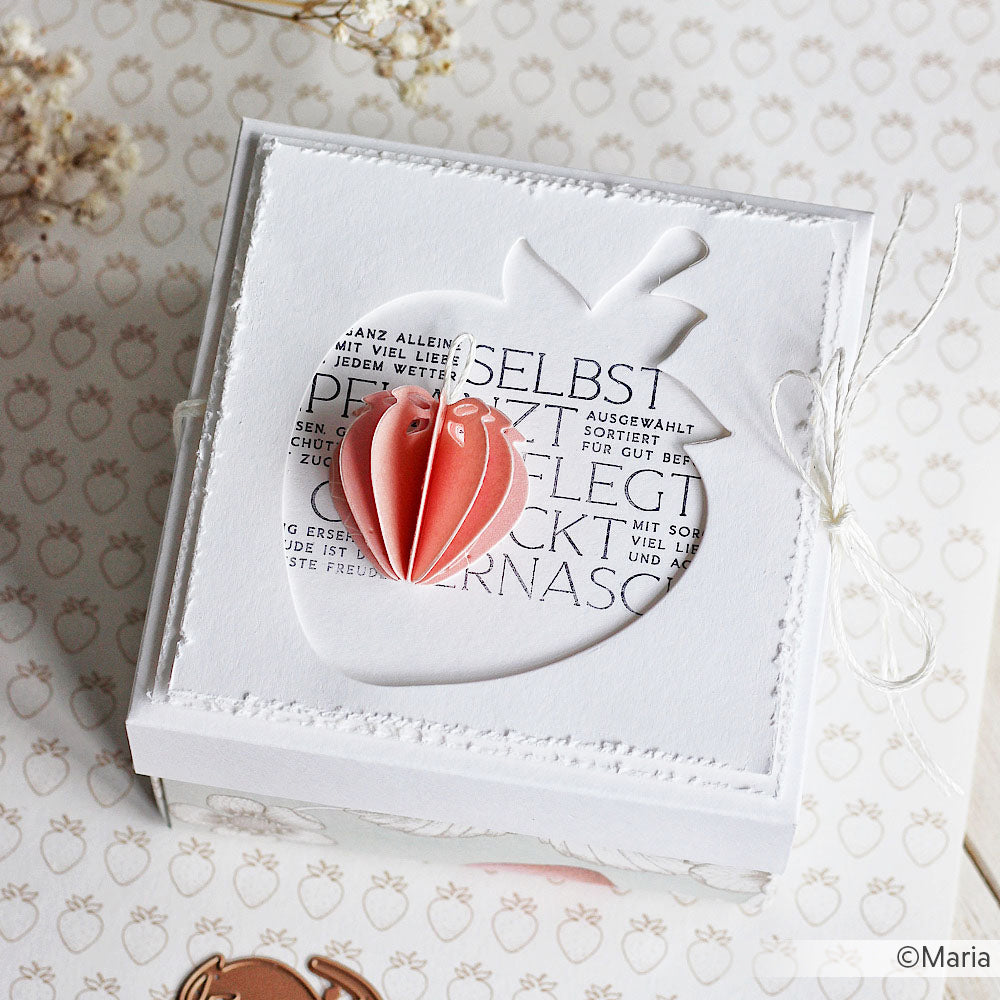 Weiße Geschenkbox mit einem Erdbeerausschnitt von Alexandra Renke, gefertigt mit Stanzsystemen und gekrönt mit einer rosa 3D-Papier-Erdbeere. Ideal, um Designpapiere in Szene zu setzen und kreatives Flair zu erzeugen.