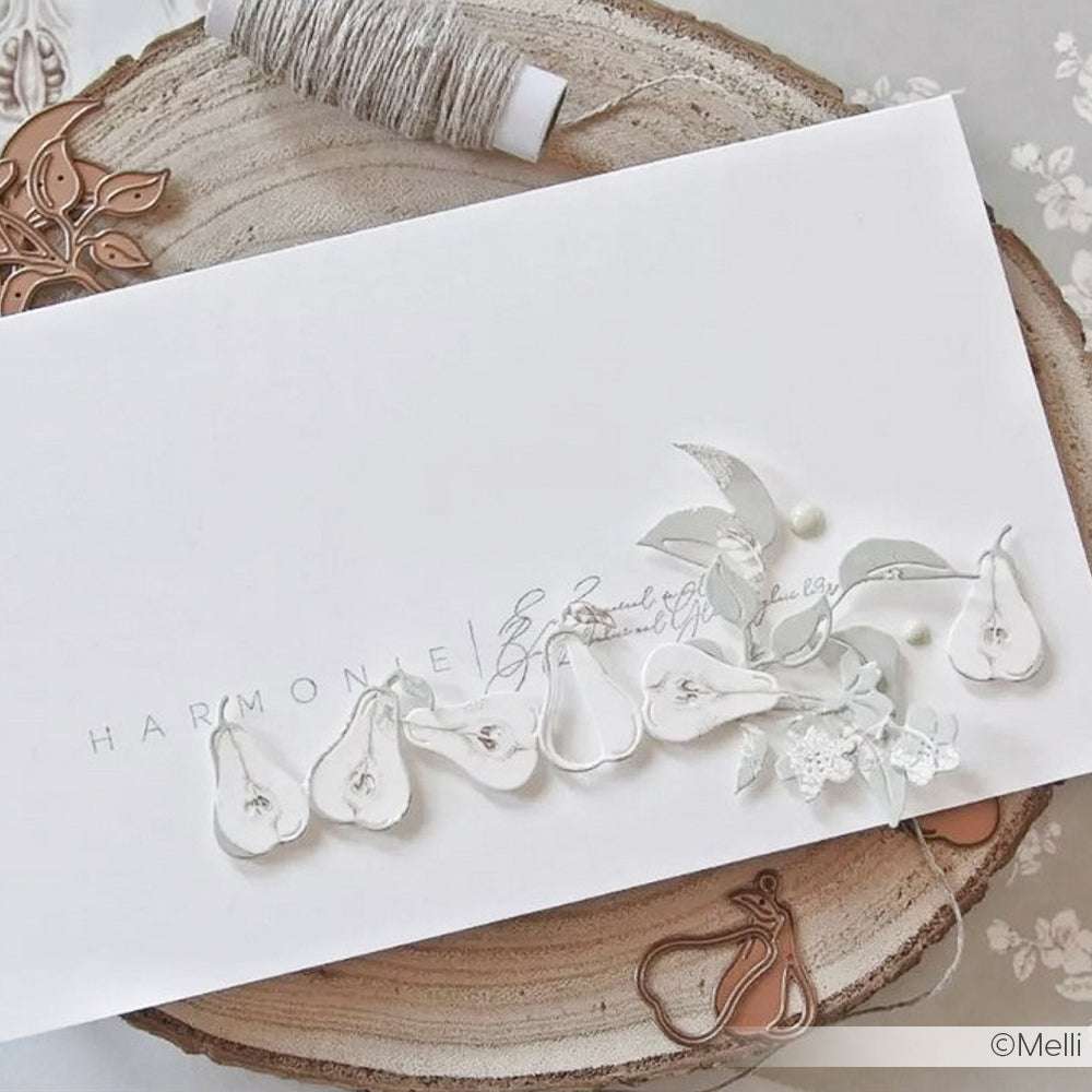 Weiße Karte von Alexandra Renke mit zarten Birnen- und Blattverzierungen, Schnurspule und Metallstempel in Birnenform - ideal für DieCut Systeme oder Stanzen für Designpapier - auf einer Holzunterlage präsentiert.