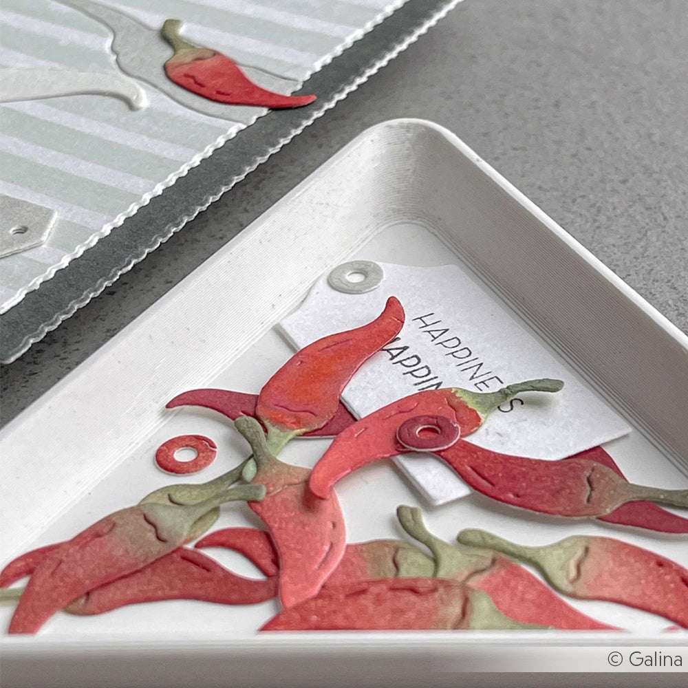 Chilischoten aus Papier, die mit dem Alexandra Renke Mini-Grill-Set hergestellt wurden, liegen in einem Tablett mit der Aufschrift HAPPINESS, daneben befinden sich bunte Teile auf einer gestreiften Alexandra Renke Designpapiere-Karte.