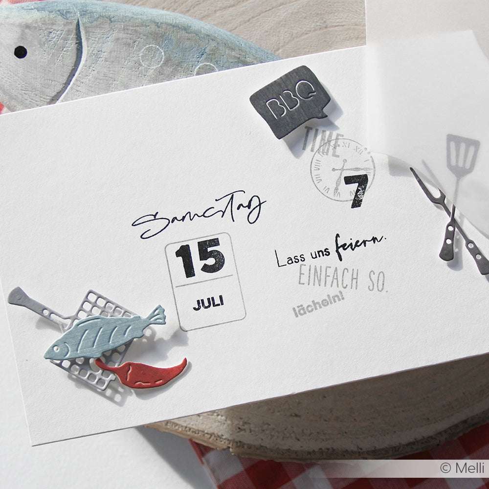 Ein Kalenderblatt für den 15. Juli mit Dekorationen zum Thema Grillen, wie einem Fisch auf einem Pfannenwender und Grillwerkzeugen, enthält lustige Details, die vom Mini-Grill-Set Motivstanze von Alexandra Renke inspiriert sind.