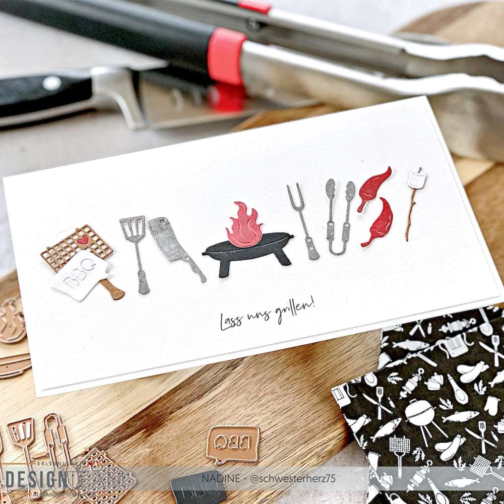 Handgefertigte Karte von Alexandra Renke mit BBQ-Motivstanze zum Ausschneiden: Mini-Grill-Set, Utensilien, Chilischoten und dem Text "Lass uns grillen!" auf weißem Hintergrund.