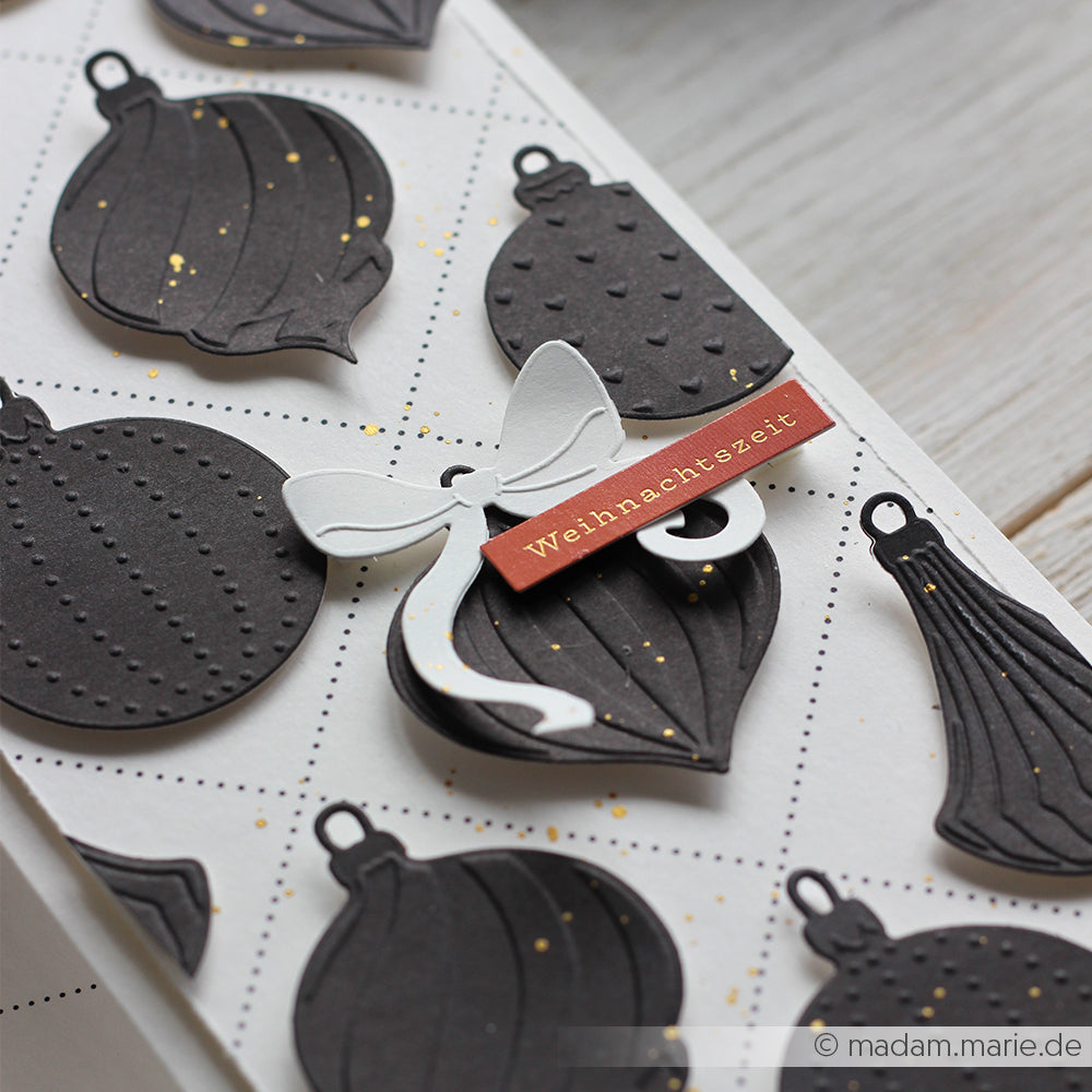 Schwarzer Weihnachtsschmuck mit goldenen Sprenkeln und einer weißen Schleife von Alexandra Renke, dazu ein rotes Weihnachtszeit-Etikett. Perfekt für Stanzsysteme oder Ihren bevorzugten Cut & Emboss Folder.