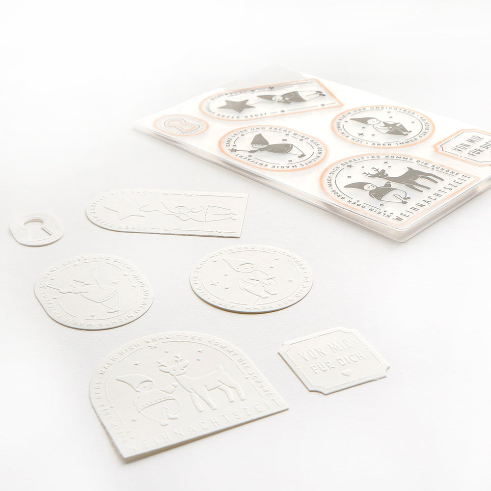 Anhänger aus weißem Prägepapier, hergestellt mit dem Schneide- und Prägefolder von Alexandra Renke und kreisförmigen Tieraufklebern, auf weißem Hintergrund.