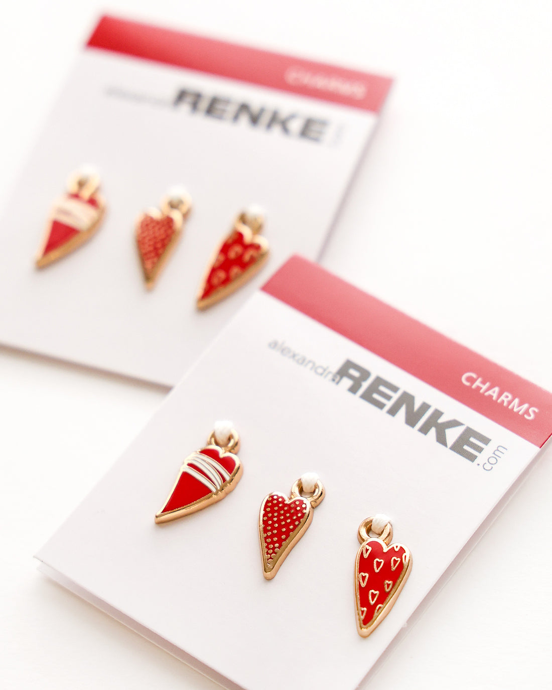 Zwei Sets mit roten und goldenen herzförmigen Anhängern auf gebrandeten Display-Karten mit der Aufschrift alexandra RENKE.