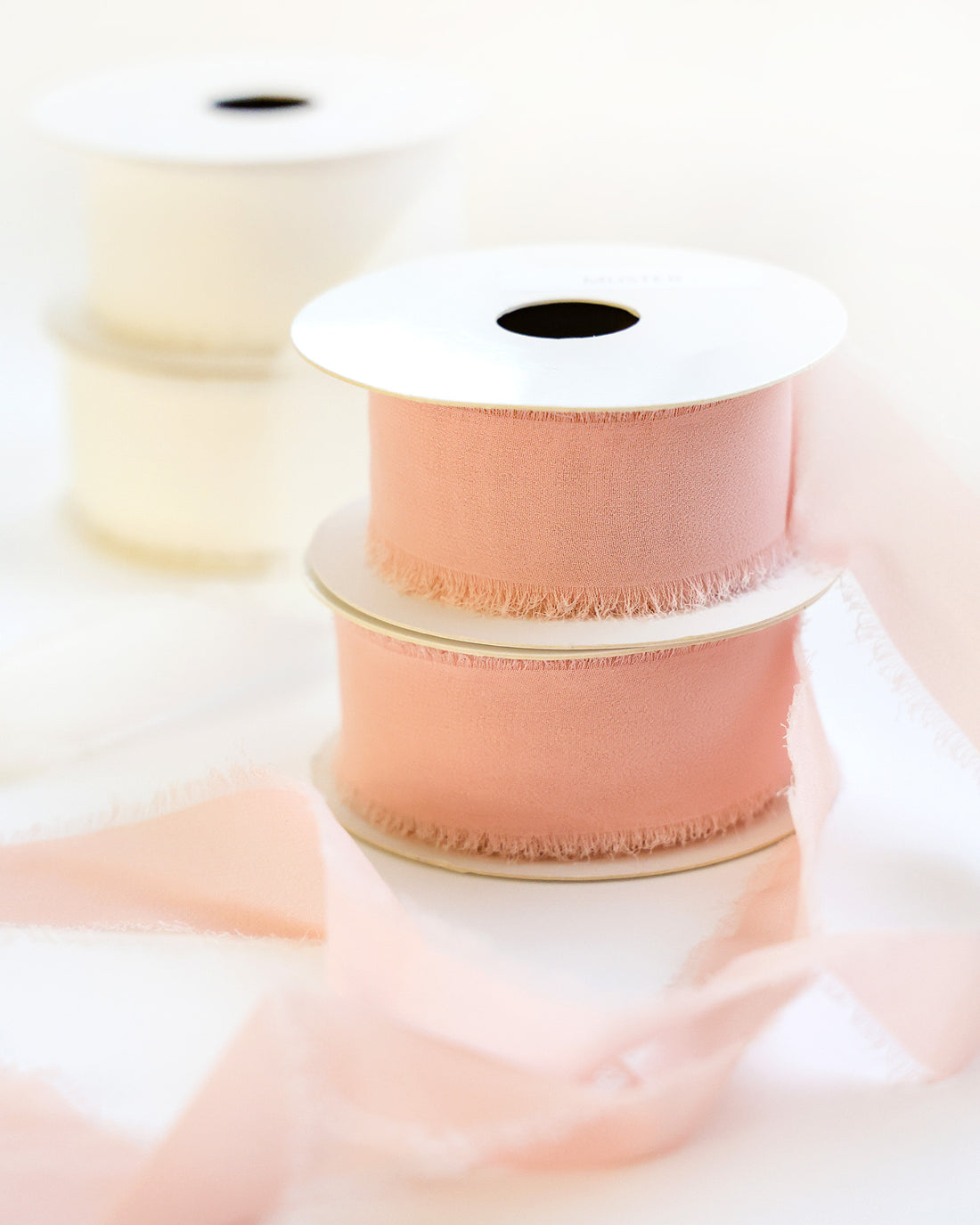 Zwei Spulen mit blassrosa Bändern gestapelt, mit einer weißen Spule und losen Bändern im Weichzeichner-Hintergrund.