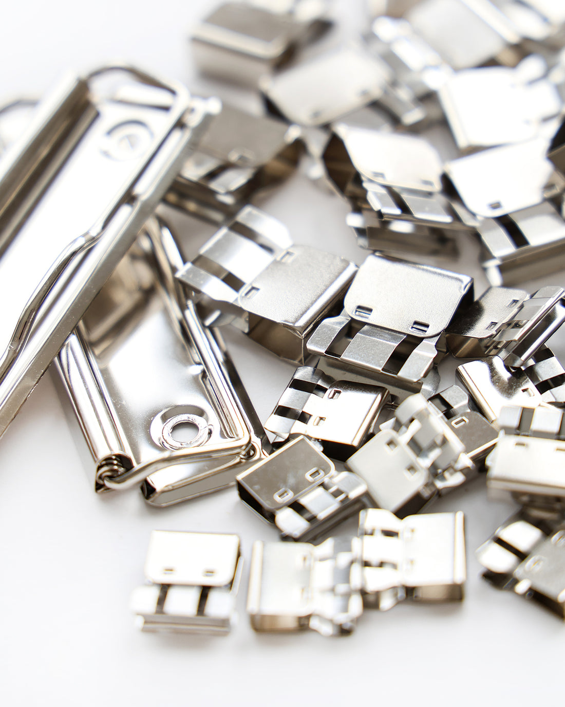 Silberne Metallklammern und -verschlüsse auf weißer Oberfläche verstreut.