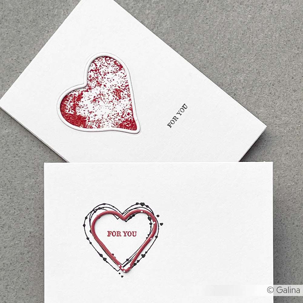 Zwei weiße Karten mit roten Herzmotiven und dem Text "FÜR DICH" liegen auf einer grauen Oberfläche. Sie wurden mit dem Photopolymer-Klarsichtstempelset von Alexandra Renke gestaltet, das für gestochen scharfe, detaillierte Abdrücke sorgt.