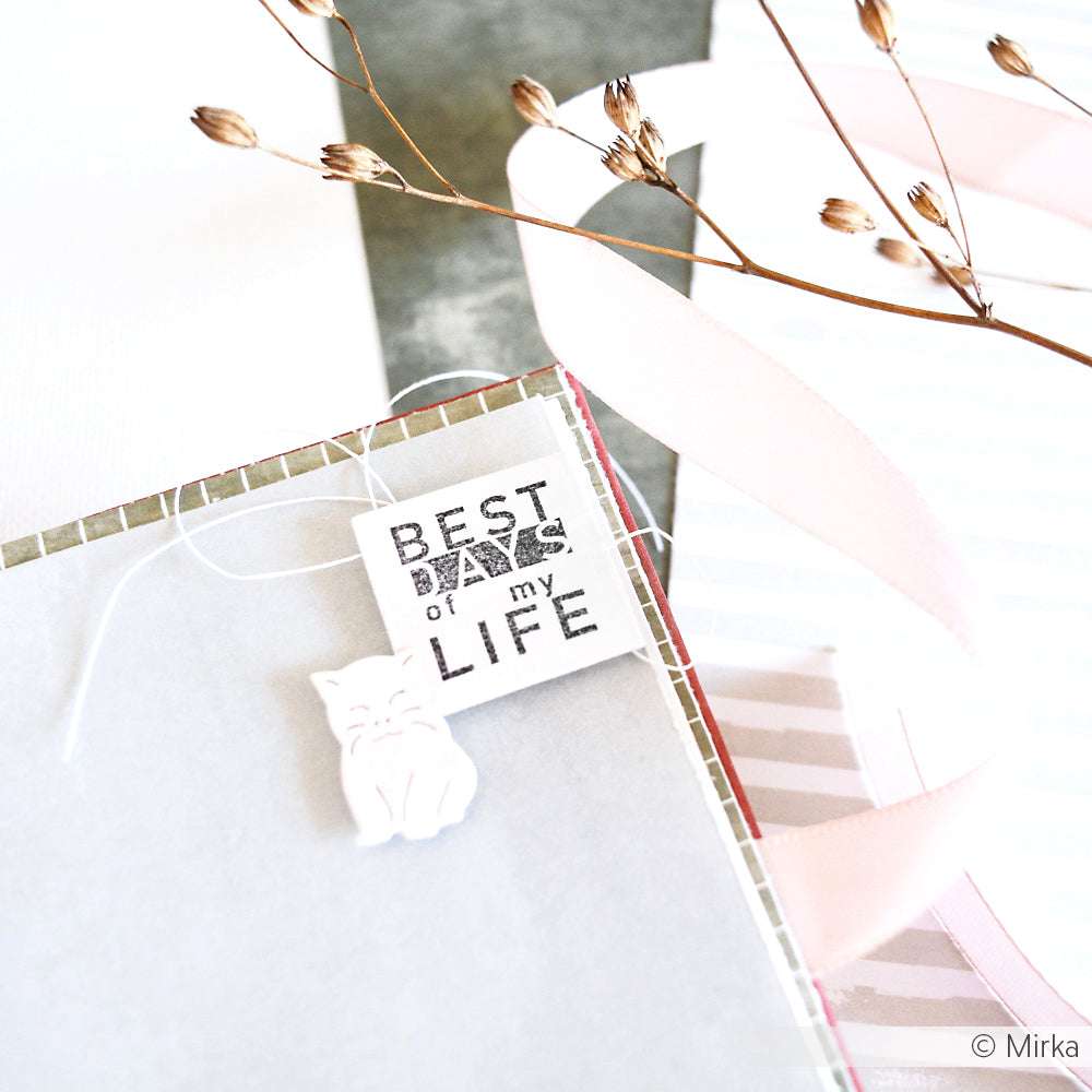 Eine bezaubernde, handgefertigte Karte mit dem Text "Die besten Tage meines Lebens", einem weißen Katzenanhänger, rosafarbenem Band, getrockneten Blumen und zarten Akzenten, die mit einem Clear Stamp Set von Alexandra Renke erstellt wurde.