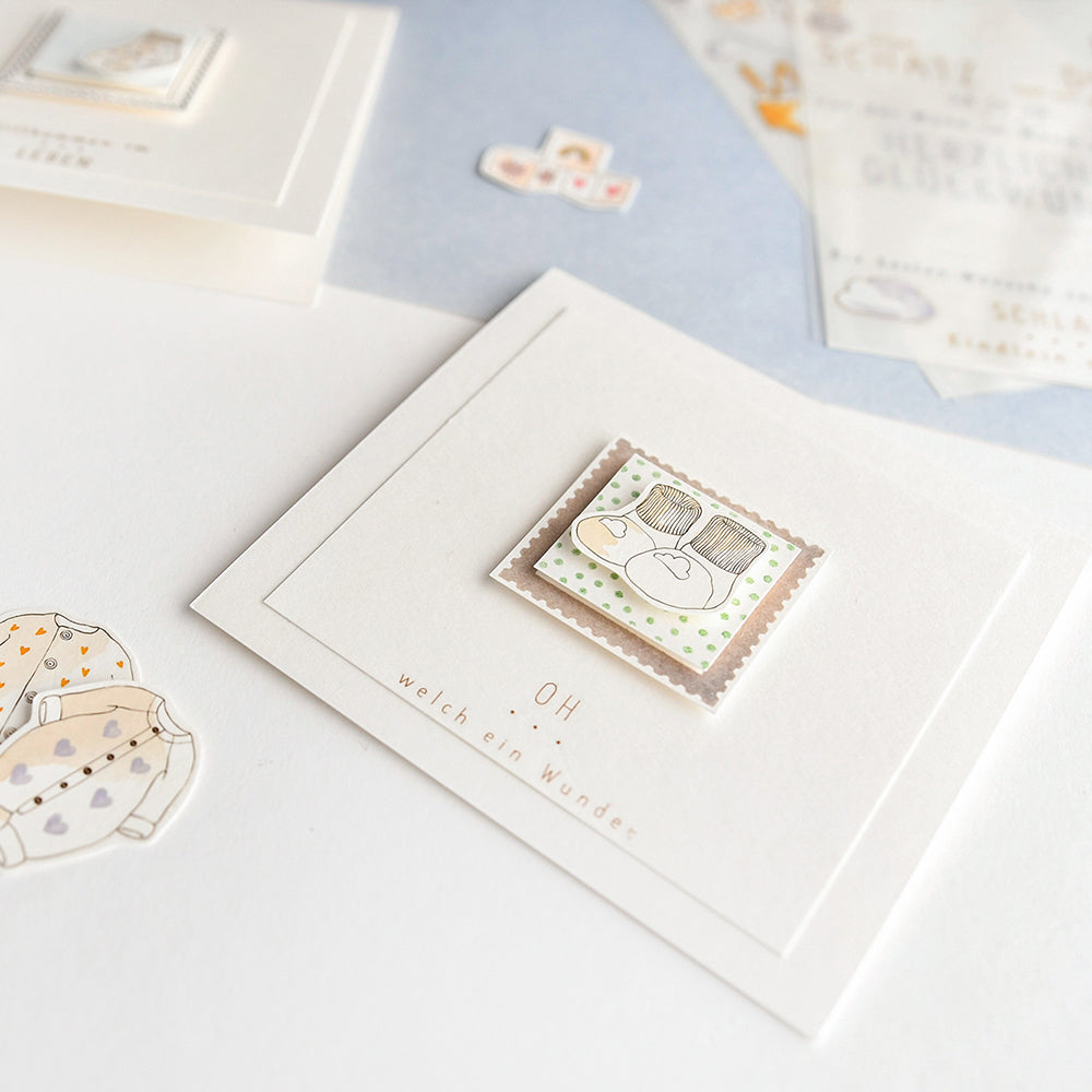 Quadratische Karte von Alexandra Renke mit einer niedlichen Illustration von Babyschuhen und Büchern, umgeben von pastellfarbenem Briefpapier - ideal zum Kombinieren mit einem klaren Stempel oder Photopolymer-Stempel für entzückende personalisierte Grüße.