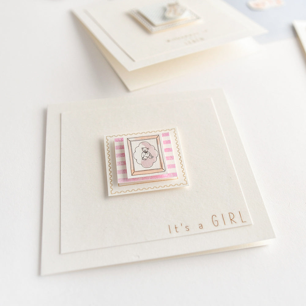 Quadratische Karte von Alexandra Renke mit einem rosa-weißen Teddybär und der Aufschrift "It's a GIRL" in der unteren rechten Ecke - eine charmante Art, die Ankunft eines neuen Kindes zu feiern.