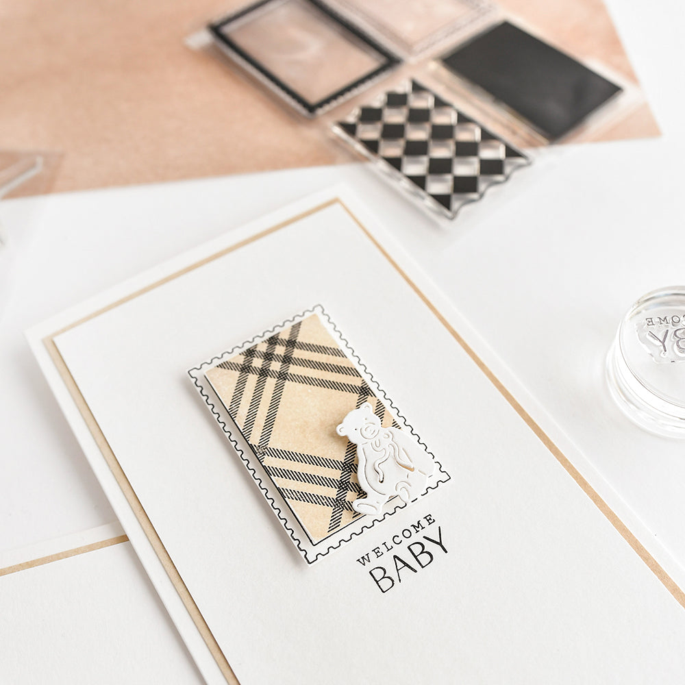 Eine handgefertigte "Welcome Baby"-Karte von Alexandra Renke mit einem karierten Design, einer kleinen weißen Bärenverzierung und einem Gruß mit Clear Stamp auf weißem Untergrund.