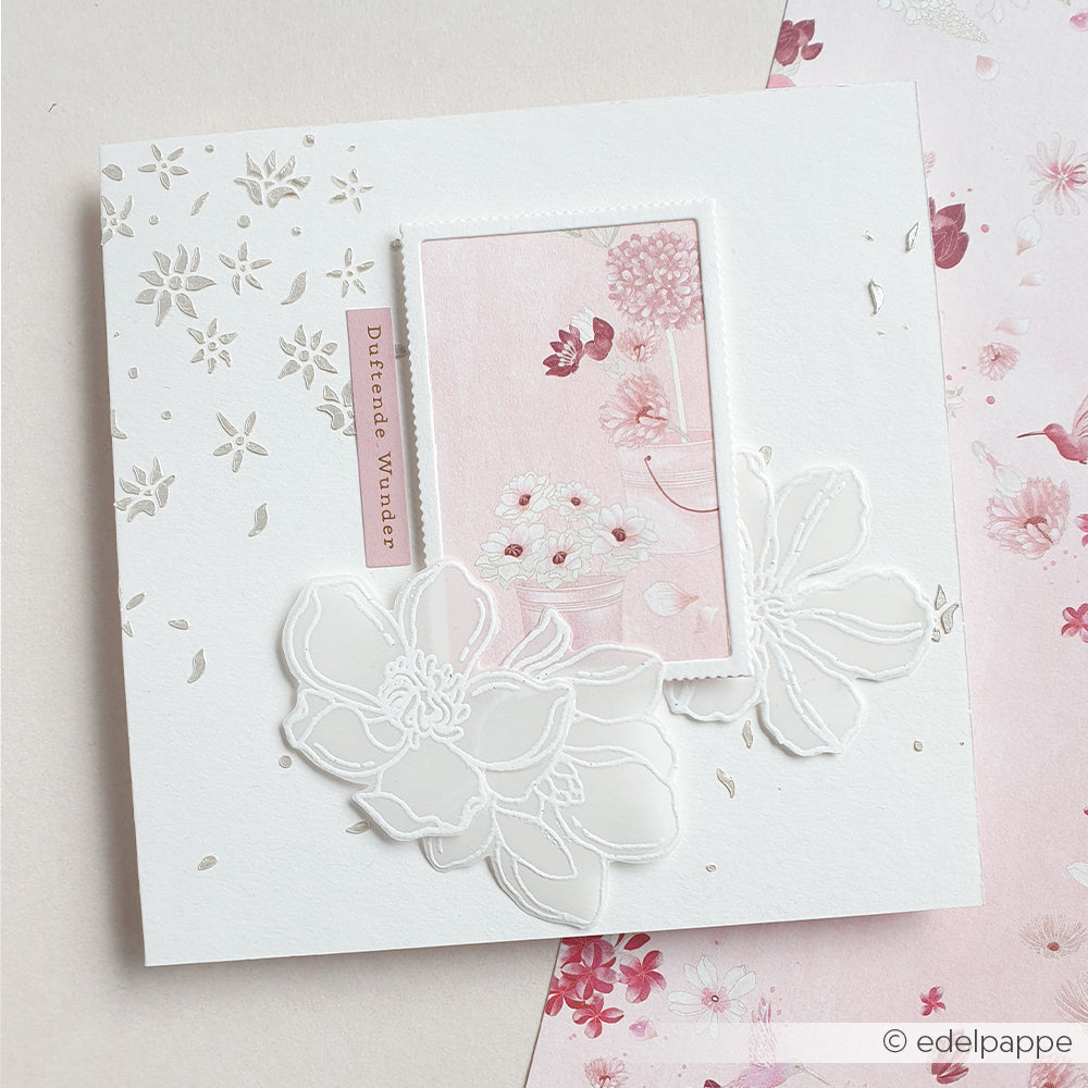 Quadratische Karte von Alexandra Renke mit weißen, geprägten Blumen, Blumenmustern und einem rosa, mit Blumen verzierten Rechteck mit der Aufschrift „Dezfrade Wunder“. Zeigt zarte „Sommerblüten“-Motive, die mit Klarsichtstempeln und Fotopolymer-Stempeln für gestochen scharfe Details gestaltet wurden.