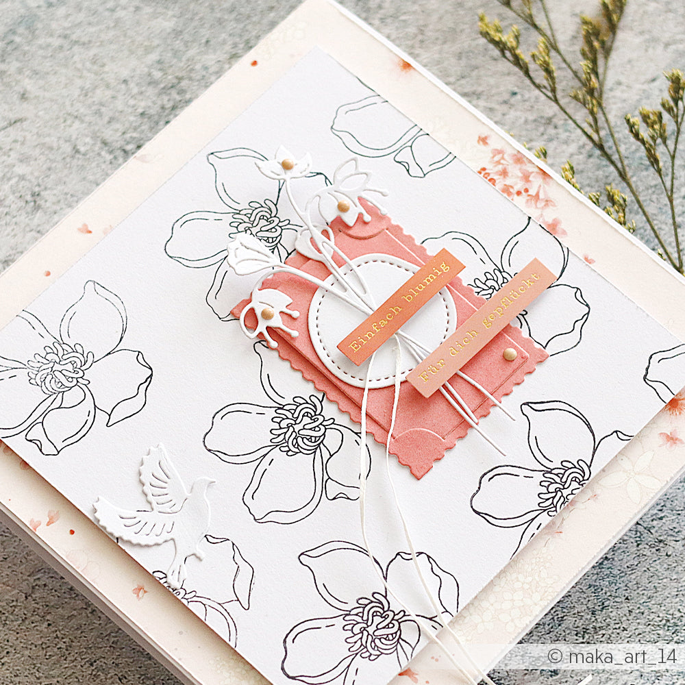 Die handgefertigte Karte von Alexandra Renke besticht durch schwarze Blumenumrisse, rosa Akzente, weiße Blüten und ein goldenes Etikett mit der Aufschrift „Blissful Pairing“, das mit dem Clear-Stempel „Sommerblüten“ gestaltet wurde und für klare, detailreiche Motive sorgt.
