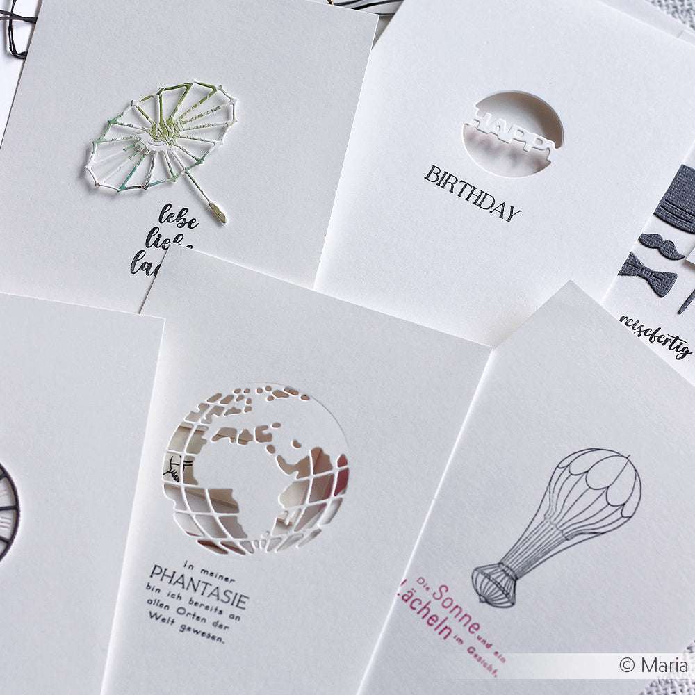 Fünf weiße Grußkarten von Alexandra Renke mit filigranen Cut-Out- und Line-Art-Motiven - Globus, Regenschirm und Luftballon - eignen sich ideal für die Kombination mit Ihren bevorzugten Clear Stamps oder Photopolymer-Stempeln für individuelle Botschaften.