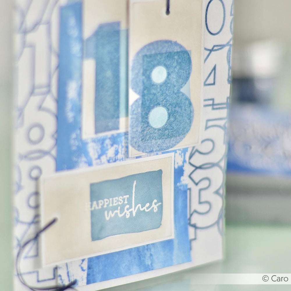 Eine handgefertigte Karte von Alexandra Renke mit den blauen Zahlen Mix-Zahlen "18" und einem Etikett auf der Vorderseite mit der Aufschrift "Glückliche Wünsche".