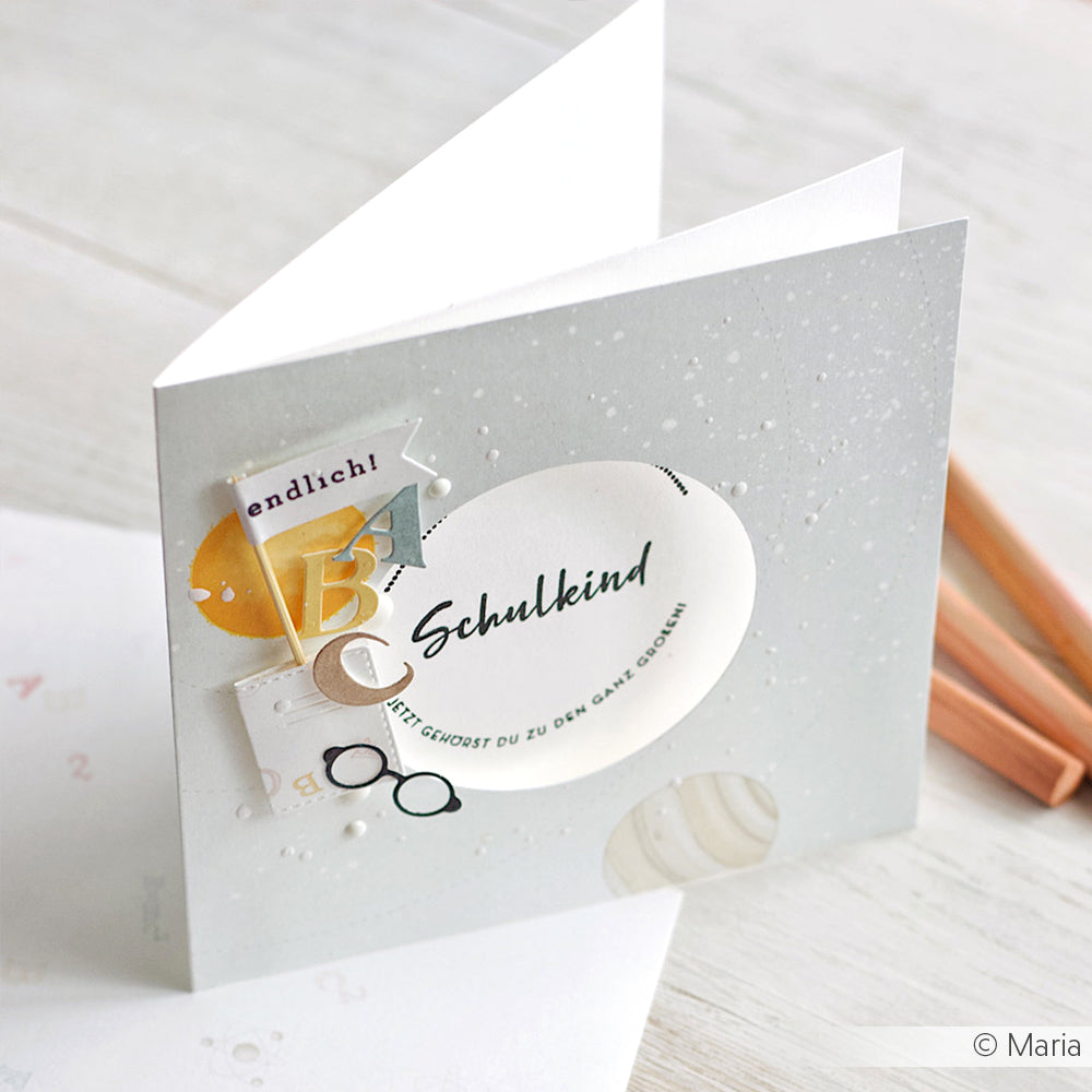 Eine Grußkarte von Alexandra Renke mit Schulkind- und Schuldekorationen wie Buchstaben, Gläsern und geometrischen Formen - ideal für die Verwendung mit dem Clear Stamp Set Schulkind oder anderen photopolymeren Stempelmotiven.