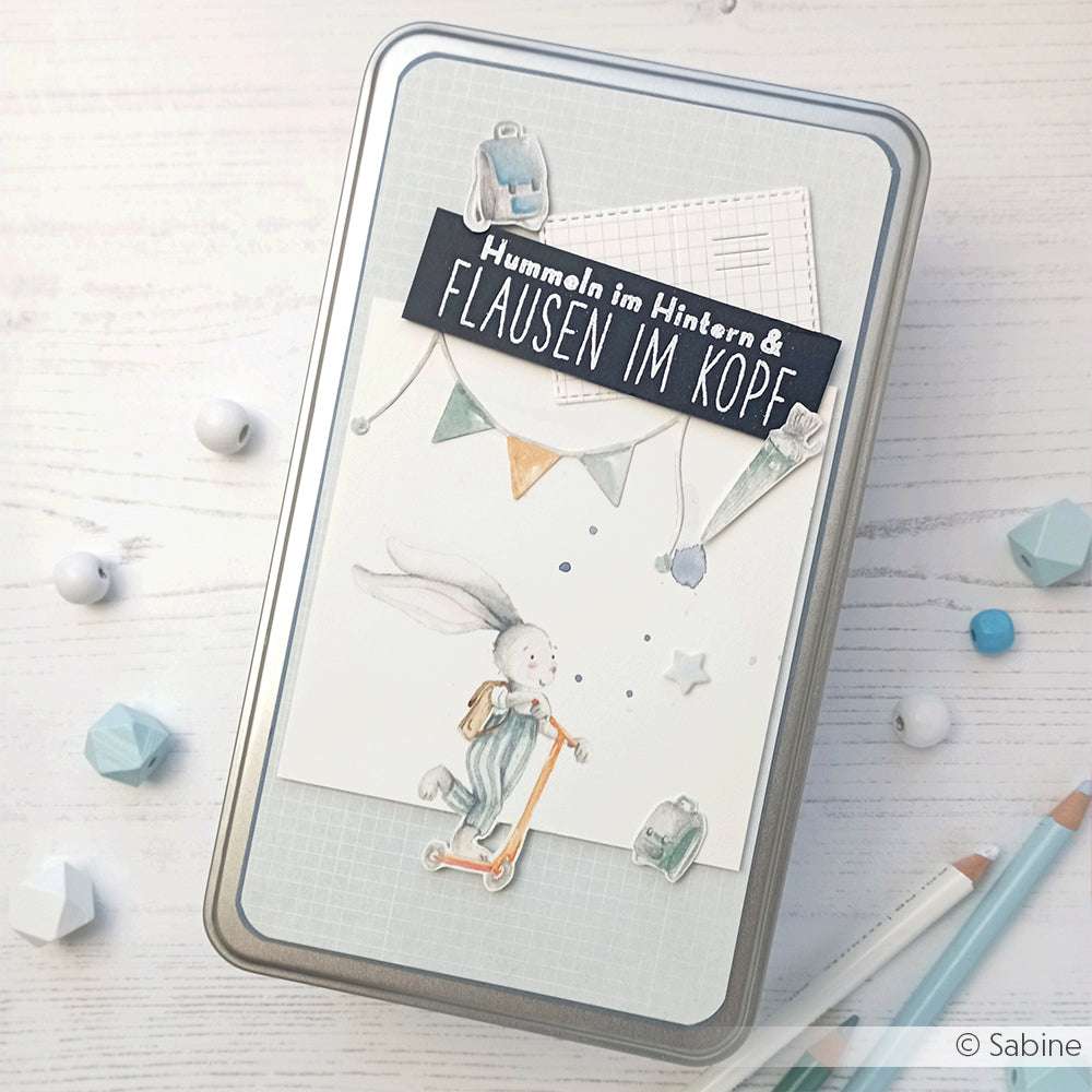 Dekorative Dose von Alexandra Renke mit einem Hasen auf einem Roller, pastellfarbenen Fähnchen und deutschem Text - ideal für Papierprojekte oder als Ergänzung zu Ihrem Lieblings-Klarstempelset.