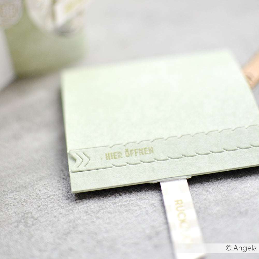 Eine hellgrüne Karte von Alexandra Renke mit der Prägung "HIER ÖFFNEN" auf einer grauen Oberfläche mit weißer Zuglasche - ideal für Kleine Botschaften oder zur Verwendung mit Ihrem Lieblings-Photopolymer-Stempel.