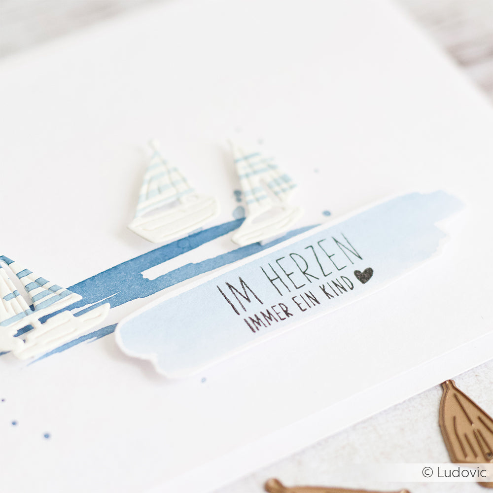Drei Papiersegelboote und der deutsche Text "IM HERZEN IMMER EIN KIND" auf einer weißen Karte mit blauen Akzenten von Alexandra Renke - ideal für Scrapbooking oder kreative Projekte mit Photopolymerstempeln und Klarsichtstempeln.