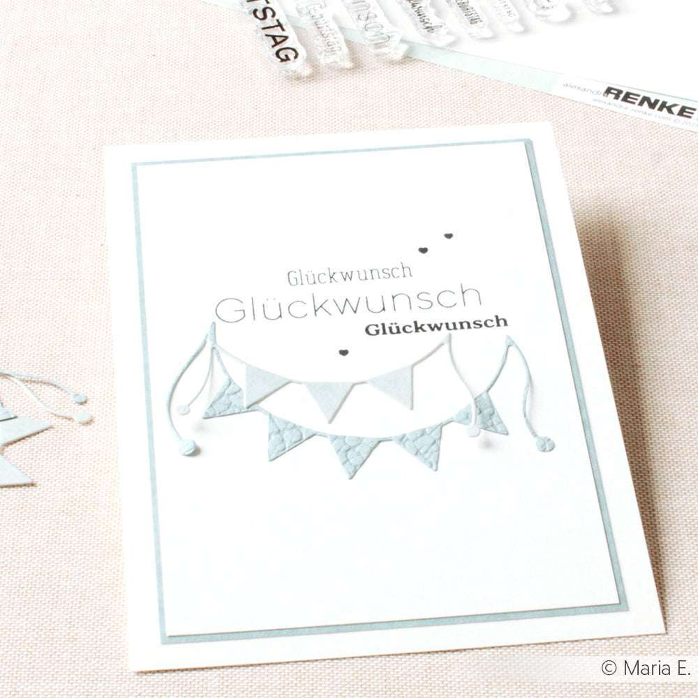 Eine Karte von Alexandra Renke mit "Herzlichen Glückwunsch" und blau-weißen Wimpeln auf beigem Hintergrund, ideal für die Kombination mit Ihren Lieblings-Photopolymerstempeln.