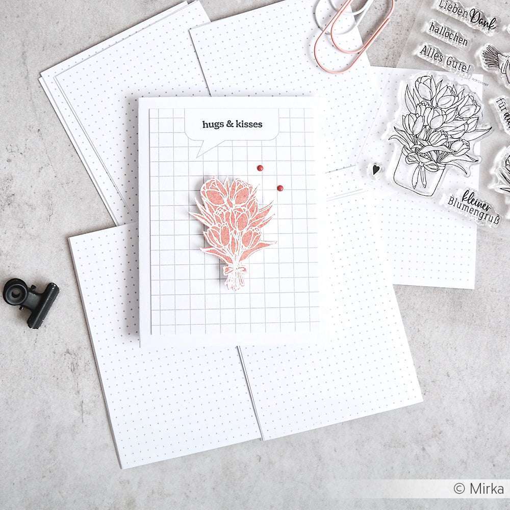 Eine handgefertigte Karte mit einer rosafarbenen Blume und dem Text "hugs & kisses", erstellt mit Alexandra Renke Clear Stamps, ist auf gepunktetem Papier inmitten verschiedener Bastelmaterialien platziert.