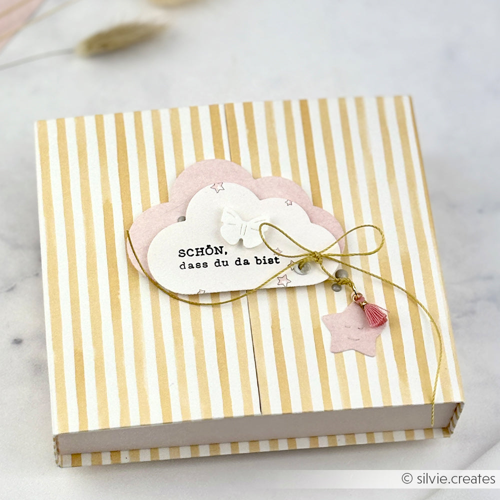 Alexandra Renke Geschenkbox mit goldenen Streifen, rosa und weißen Wolkenausschnitten, Sternanhänger, deutschem Text und einem Photopolymer-Stempel "It's a boy" für eine besondere Note.