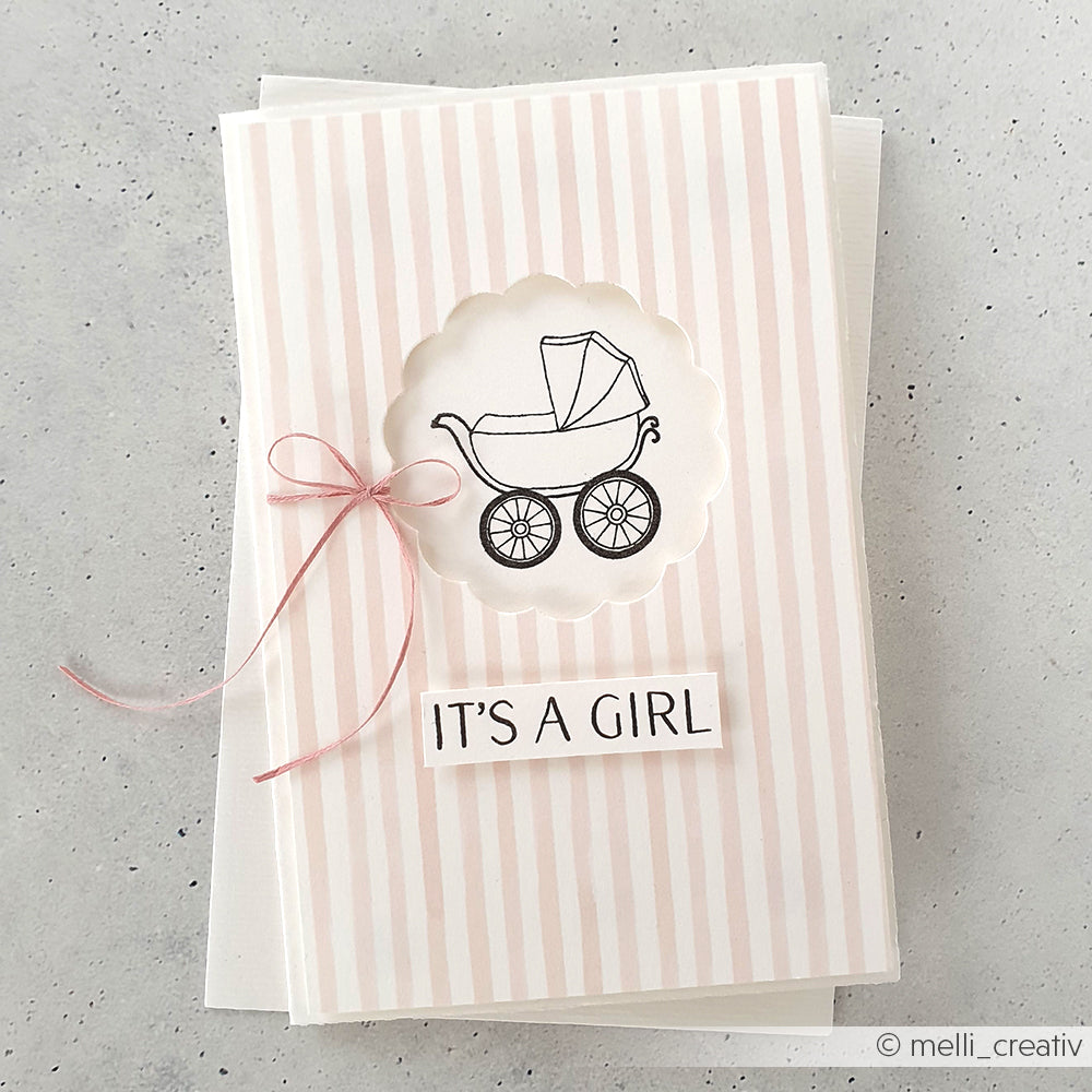 Rosa-weiß gestreifte Karte von Alexandra Renke mit einem illustrierten Kinderwagen, einer rosa Schleife und dem Text "It's a girl", der mit einem Clear Stamp gestempelt wurde, um die Details hervorzuheben.