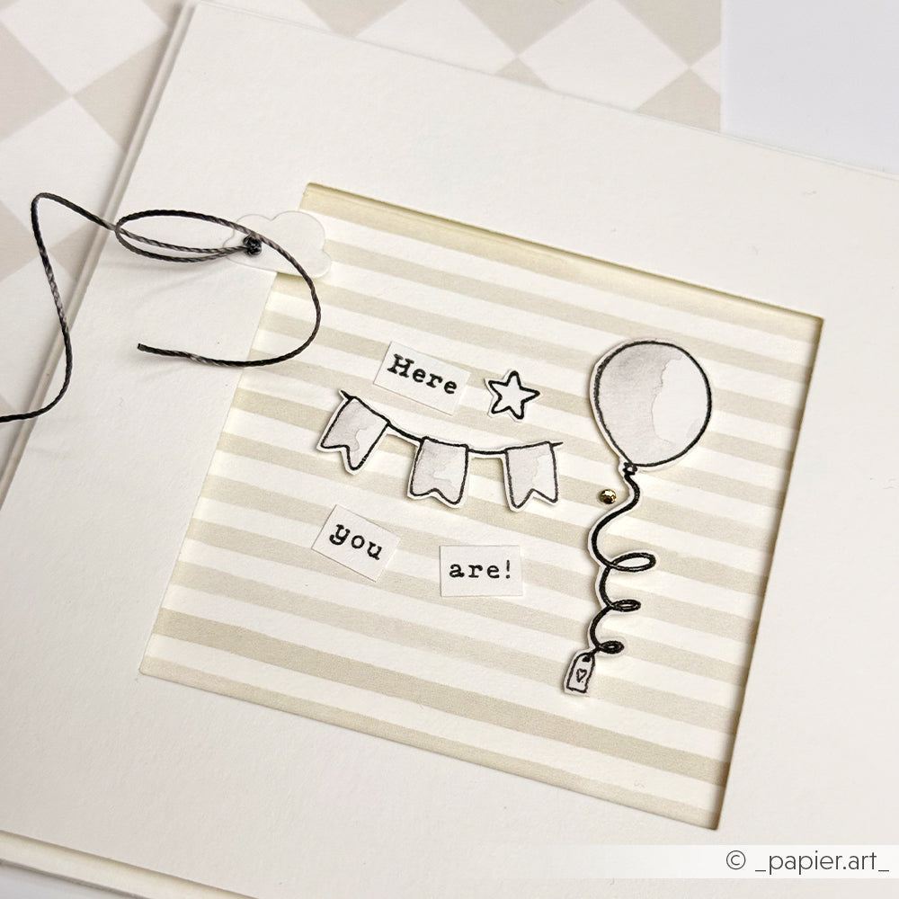Handgefertigte Karte mit einem Ballon, einer Wimpelkette und einem Stern mit der Aufschrift "Here you are!" auf einem beigefarbenen gestreiften Hintergrund, gestaltet mit klaren Stempeldetails aus der Kollektion Welcome Baby von Alexandra Renke.