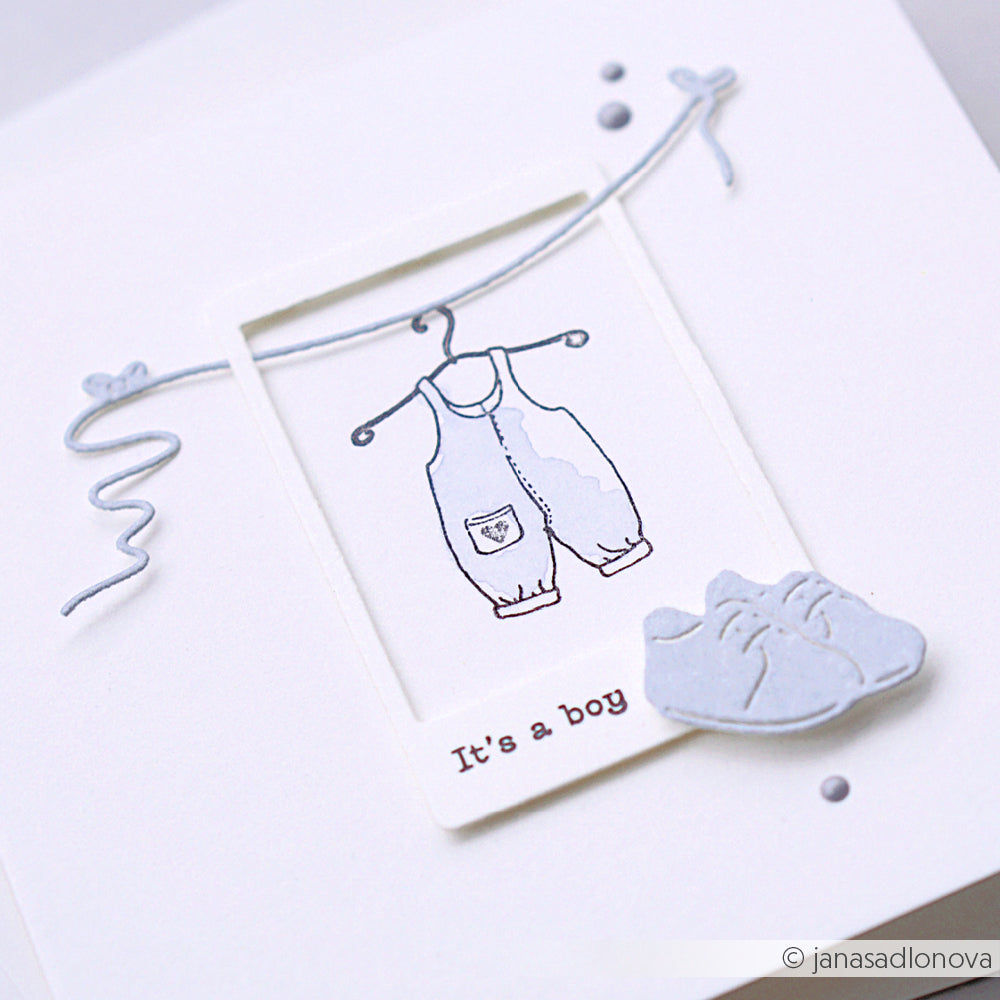 Die weiße Karte von Alexandra Renke zeigt einen blauen Baby-Overall auf einem Bügel, winzige Schuhe und den Text "It's a boy" - ideal für Komposition Welcome Baby-Projekte oder zur Verwendung mit Ihrem Lieblings-Photopolymer Stempel Clear Stamp.