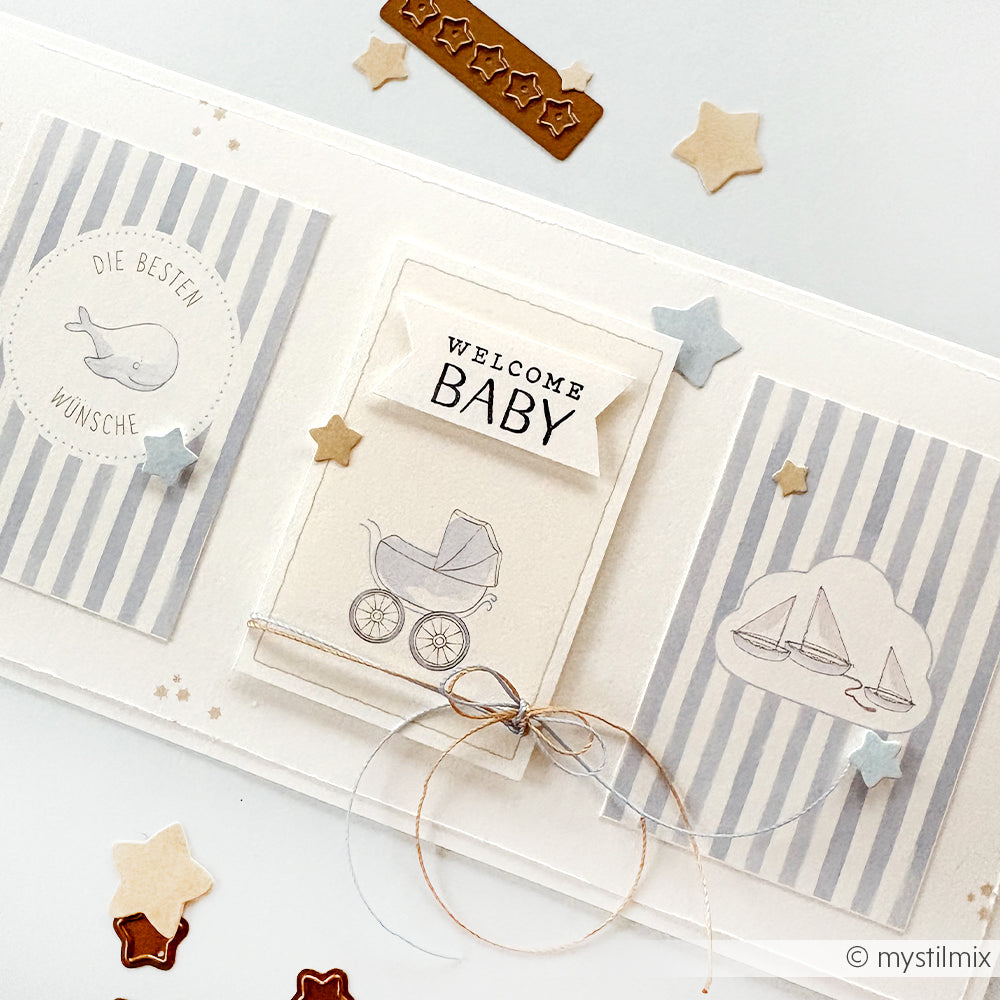Eine handgefertigte Babykarte mit dem Schriftzug "Welcome Baby", Sternenformen und sanften blau-beigen Illustrationen, hergestellt mit dem Alexandra Renke Welcome Baby Clear Stamp für klare, sanfte Details.