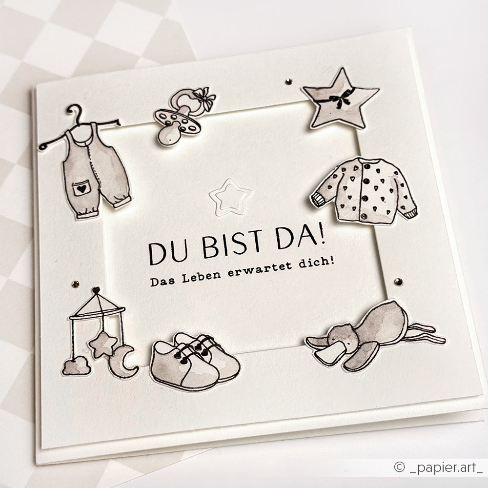 Handgefertigte Babykarte von Alexandra Renke mit deutschem Text und Photopolymer-Stempel, verziert mit niedlichen Babyartikeln wie Kleidung, Schuhen und Spielzeug - ideal für Ihre besonderen Papierprojekte.