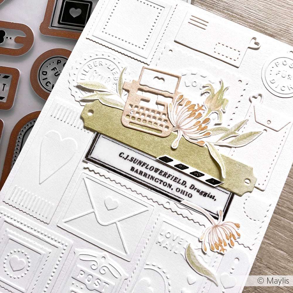 Handgemachte Karte mit geprägten Postmotiven und Blumen, gestaltet mit Alexandra Renke Designpapieren und einer alten Schreibmaschine aus dem Motivstanze Schreibmaschinen Set über einem Namensetikett.