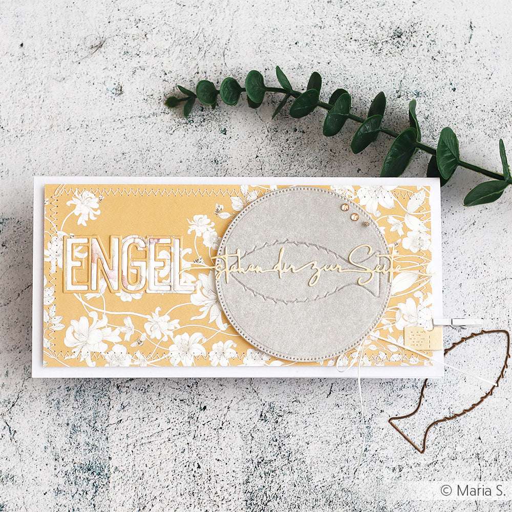 Handgefertigte gelbe und weiße Blumenkarte mit dem Text "ENGEL", hergestellt mit der Motivstanze Engel von Alexandra Renke und mit runden Stichen verziert, neben einem grünen Pflanzenzweig.