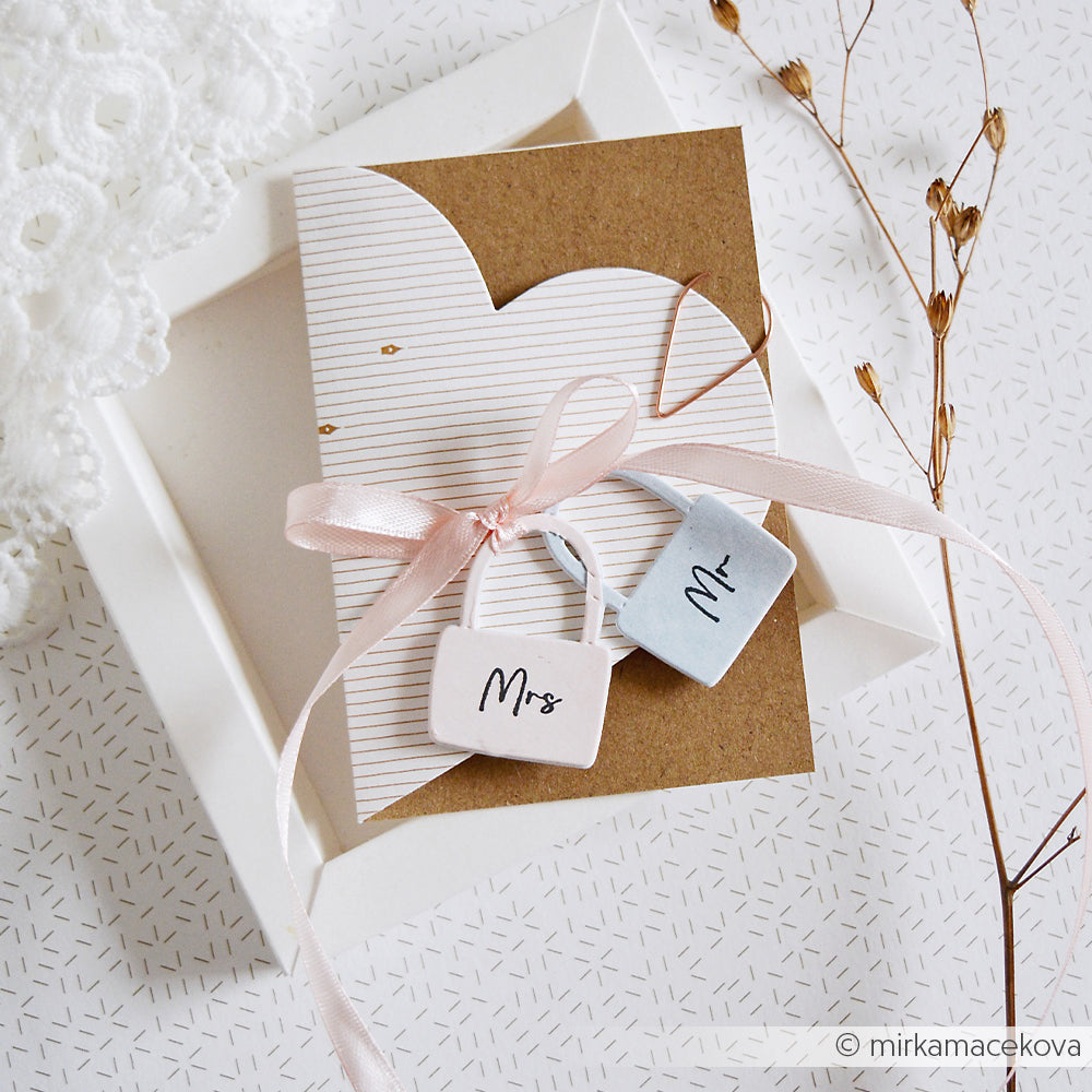Eine Hochzeitskarte von Alexandra Renke aus feinem Designpapier mit gestanztem Herzmotiv, rosafarbenem Band und Mr. & Mrs. Anhängern, wunderschön präsentiert in einer weißen Schachtel.