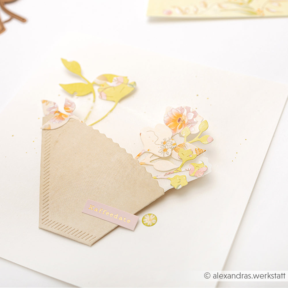 Eine handgefertigte Karte von Alexandra Renke aus feinem Designpapier mit Blumenausschnitten, die mit einer Kaffeefilterstanze ausgestanzt wurden, in einem braunen Umschlag mit der Aufschrift "Kaffeepause".