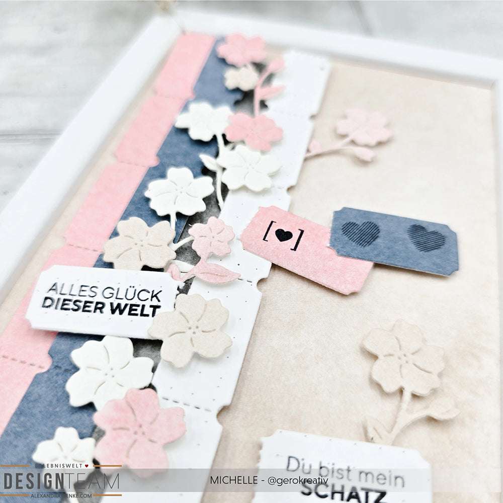 Eine handgemachte Karte von Alexandra Renke mit pastellfarbenen Blumen, Papierstreifen von Designpapiere und deutschem Text auf beigem Hintergrund.