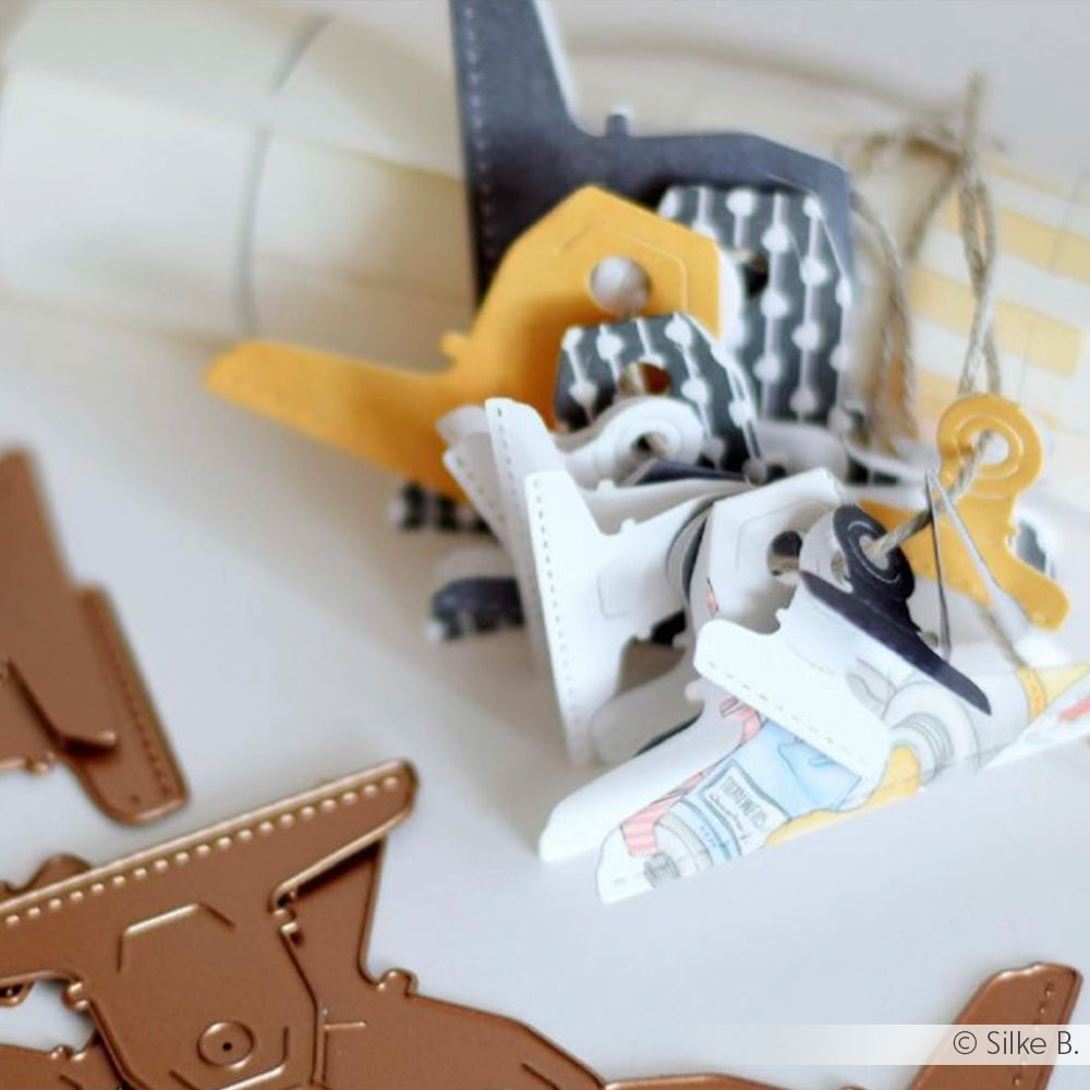Eine Nahaufnahme von bunten Papierflugzeugausschnitten, Alexandra Renke Designpapieren und Metallstempeln, die auf einer weißen Fläche angeordnet sind.