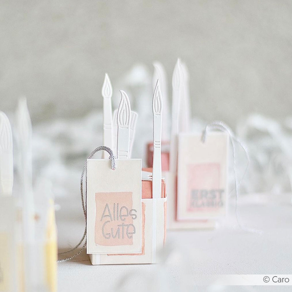 Kleine pastellfarbene Geschenkschachteln mit Papierkerzen und Anhängern - auf einer steht "Alles Gute" -, die mit Alexandra Renke Stanzsystemen und Motivstanze Pinsel hergestellt wurden, sorgen für eine sanfte, leichte Atmosphäre.