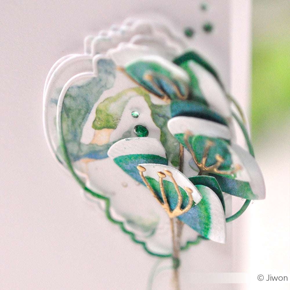 Eine Nahaufnahme der mit Alexandra Renke Designpapiere und DieCut Systeme hergestellten Aquarellblumen, mit grünen und goldenen Akzenten auf weißem Hintergrund.