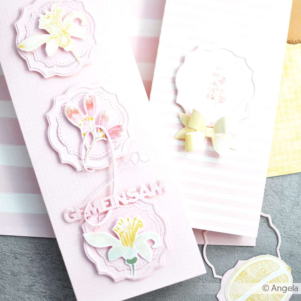 Rosa handgefertigte Karte mit floralen Verzierungen aus Alexandra Renke Designpapieren und dem Text GENIESAM, neben einer gestreiften Karte. Verziert mit Stanzsystemen und dem Motivstanze Schmucketikett Wien für zusätzlichen Charme.