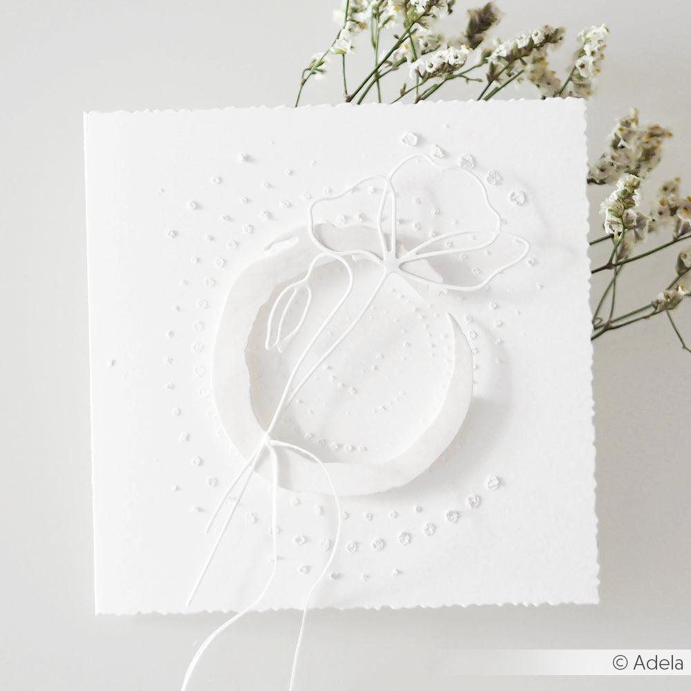 Diese weiße Prägekarte von Alexandra Renke ist aus hochwertigem Designpapier gefertigt und zeigt eine zarte abstrakte Blume mit kleinen weißen Blüten auf hellem Hintergrund, akzentuiert durch die einzigartige Maru Kreis Motivstanze.