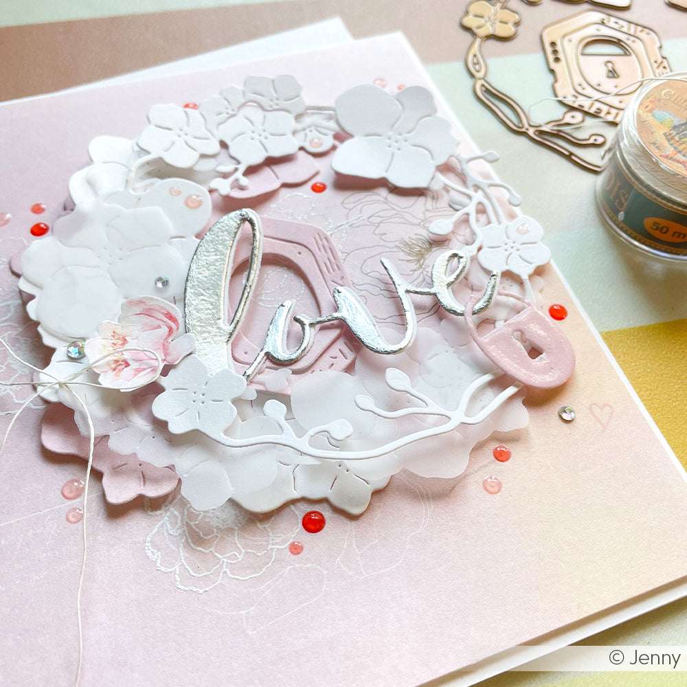 Handgefertigte Karte von Alexandra Renke mit weißen und rosafarbenen Blumen, Perlen und "Liebe" in silberner Schrift auf einem pastellfarbenen Hintergrund, hergestellt mit DieCut Systemen und 100% Stahlstanzen für komplizierte Details.