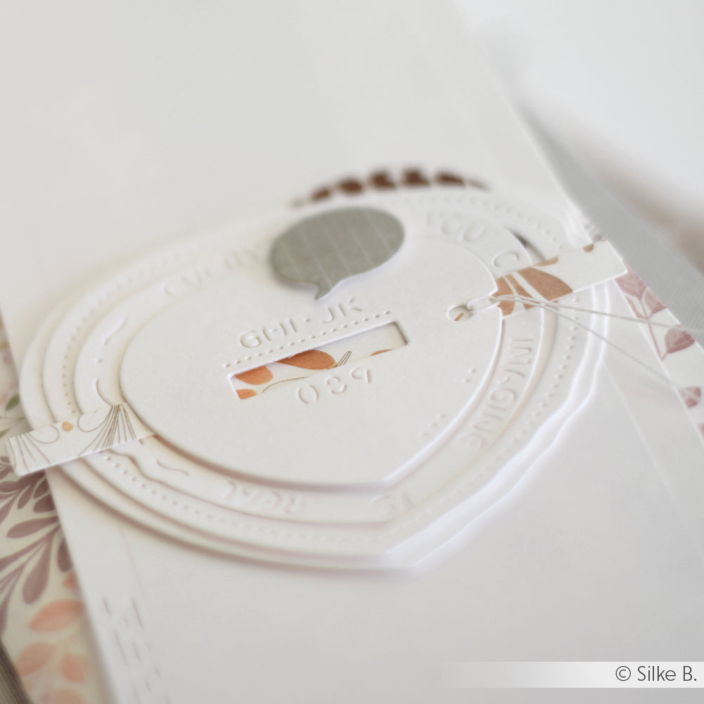 Nahaufnahme einer geprägten Karte aus weißem Papier, die mit Alexandra Renke DieCut Systemen hergestellt wurde, mit ausgestanzten Details und einem dekorativen Blumenstreifen.