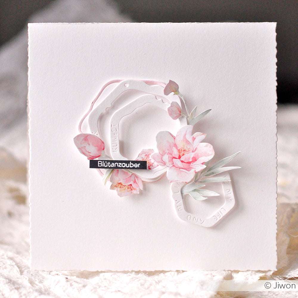 Eine weiße quadratische Karte von Alexandra Renke mit rosa Blumen, zarten Ausschnitten und dem Wort "Blütenzauber".
