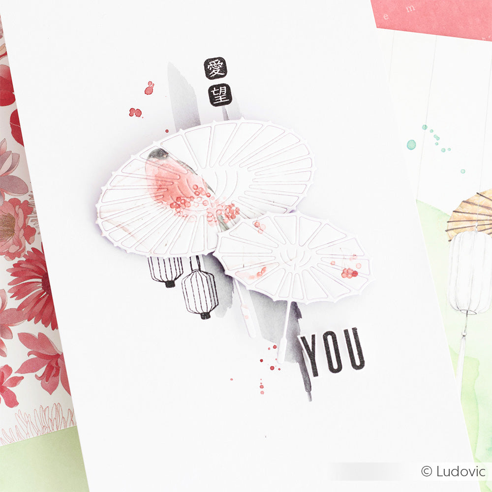 Minimalistische Karte von Alexandra Renke aus Designpapier, verziert mit zwei weißen Sonnenschirmen aus der Stanze "Motivstanze Sonnenschirm groß", rosa Blumenakzenten und dem Schriftzug YOU sowie asiatischen Schriftzeichen.