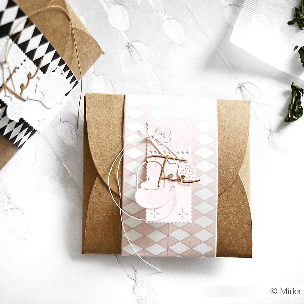 Eine braune Geschenkschachtel mit einem rosafarbenen und weißen Rautenband und einem zarten Schlittschuhdekor, hergestellt mit Alexandra Renke DieCut Systemen und Stanzen aus Stahl.