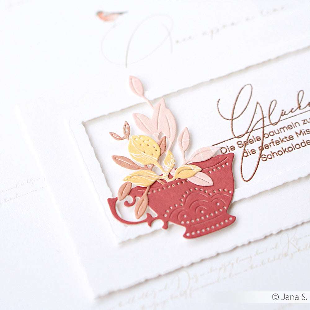 Eine rote Teetasse mit pastellfarbenen Papierblumen sitzt auf einer eleganten weißen Karte mit kursivem Text - gefertigt aus feinen Alexandra Renke Designpapieren für einen stilvollen Touch.