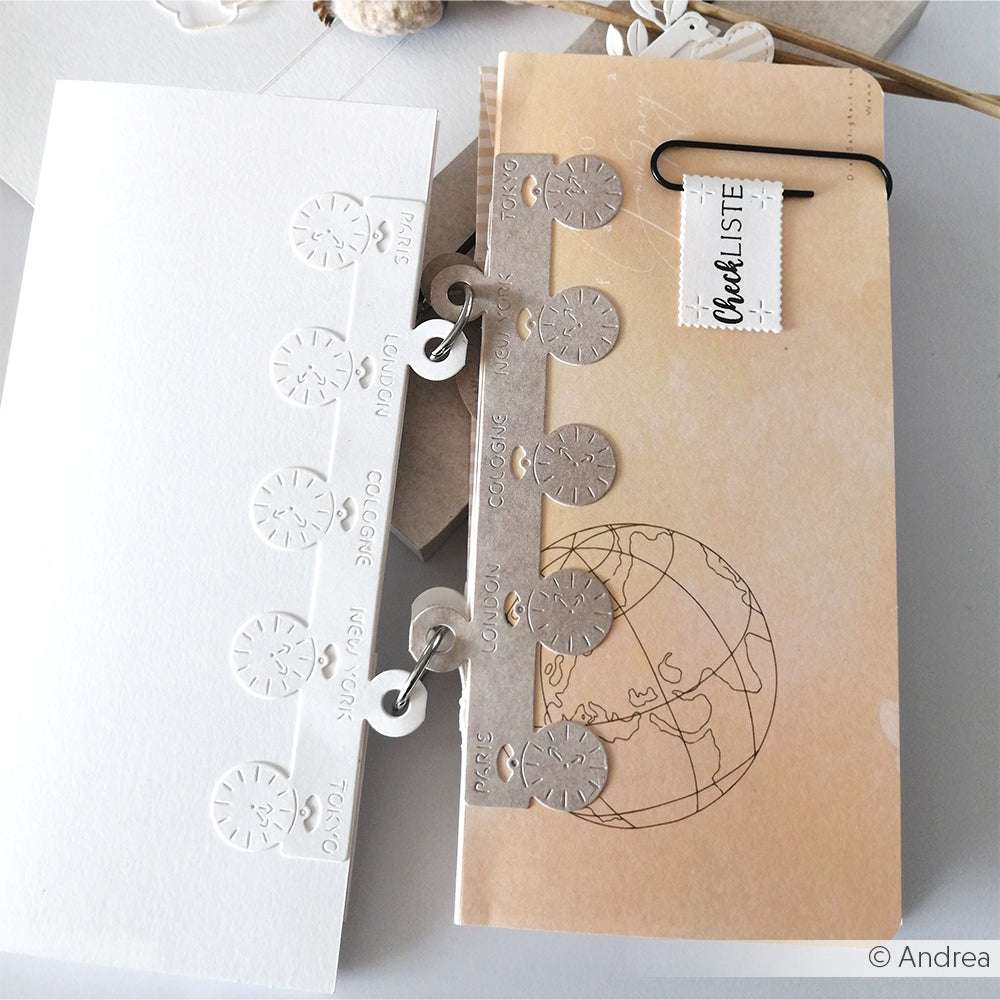 Zwei Notizbücher von Alexandra Renke zum Thema Reisen, eines in Weiß und eines in Beige, sind mit kreisförmigen DieCut-System-Ausschnitten und einer Weltkarte für stilvolle Abenteuer versehen.