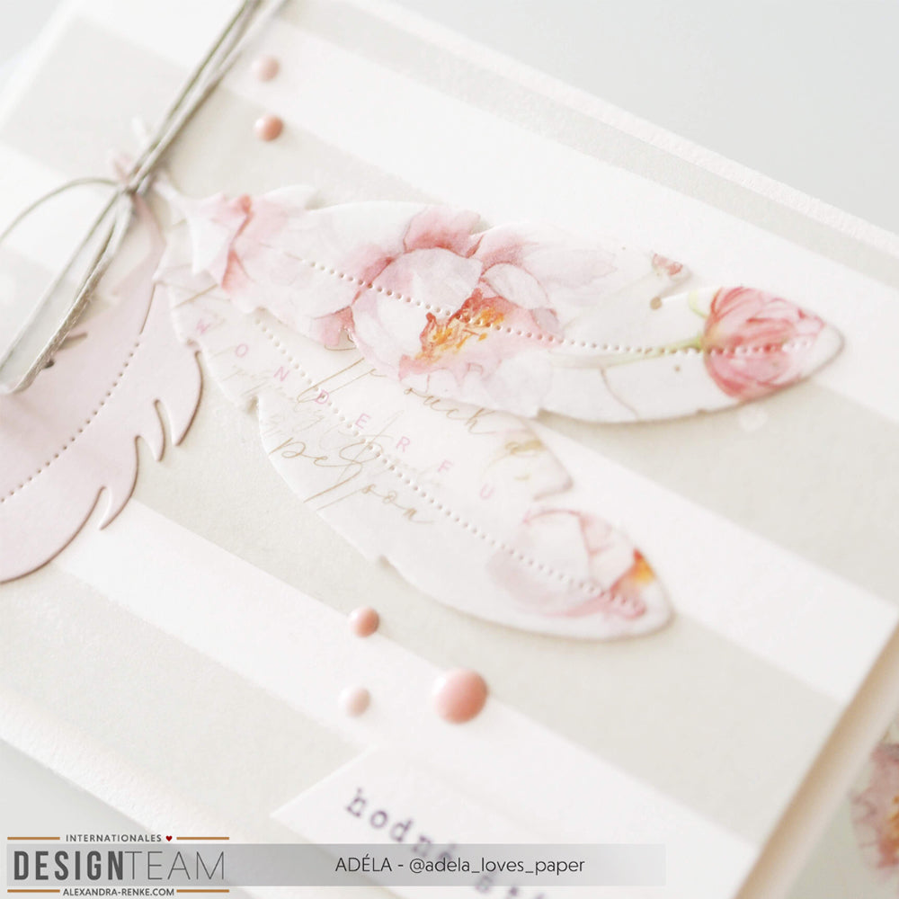 Eine handgefertigte Karte mit rosafarbenen, floralen Federausschnitten, die mit Alexandra Renke Motivstanze Feder, pastellfarben gestreiftem Designpapier und dekorativen Punkten gestaltet wurde.
