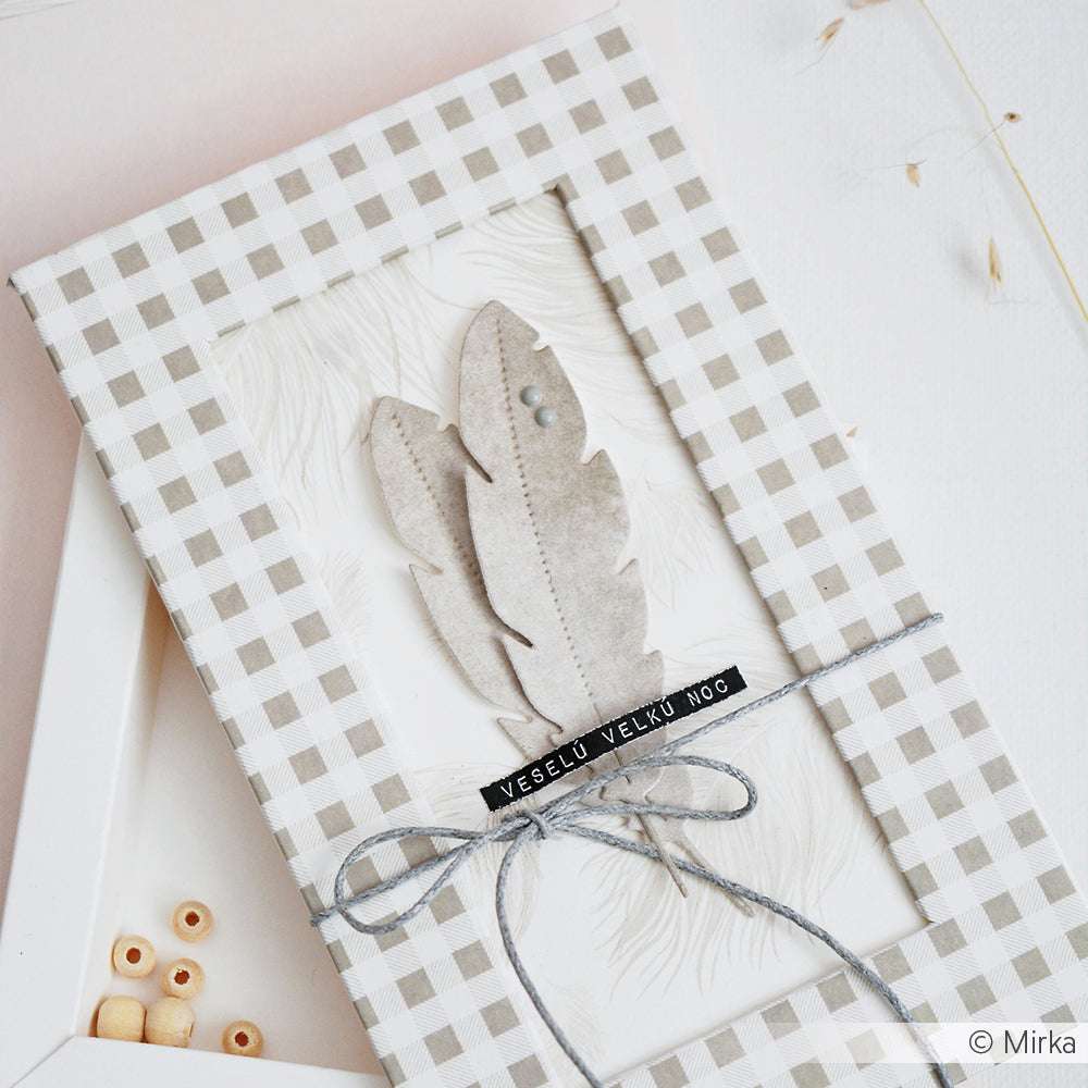 Eine karierte, mit Federn verzierte Geschenkschachtel, die mit der Motivstanze Feder 3 von Alexandra Renke hergestellt, mit Schnur gebunden und mit VEEELU VELKU NOC beschriftet wurde.